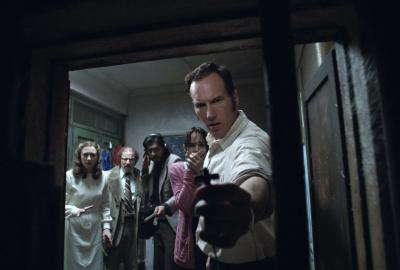 Ed holds a crucifix through a door.