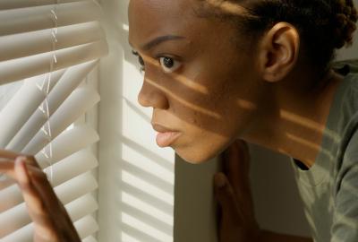 A paranoid woman peeks through closed blinds