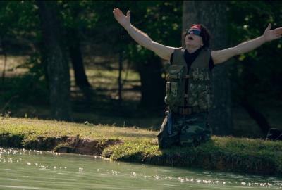 A man by the river holds his arms up to the sky