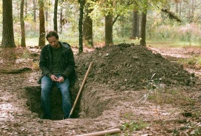 A man sites by a freshly dug gravesite.